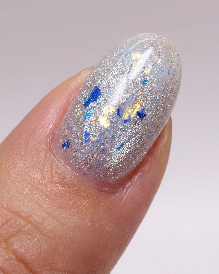 A brush applying a smooth layer of glossy top coat over a nail decorated with glitter flakes.