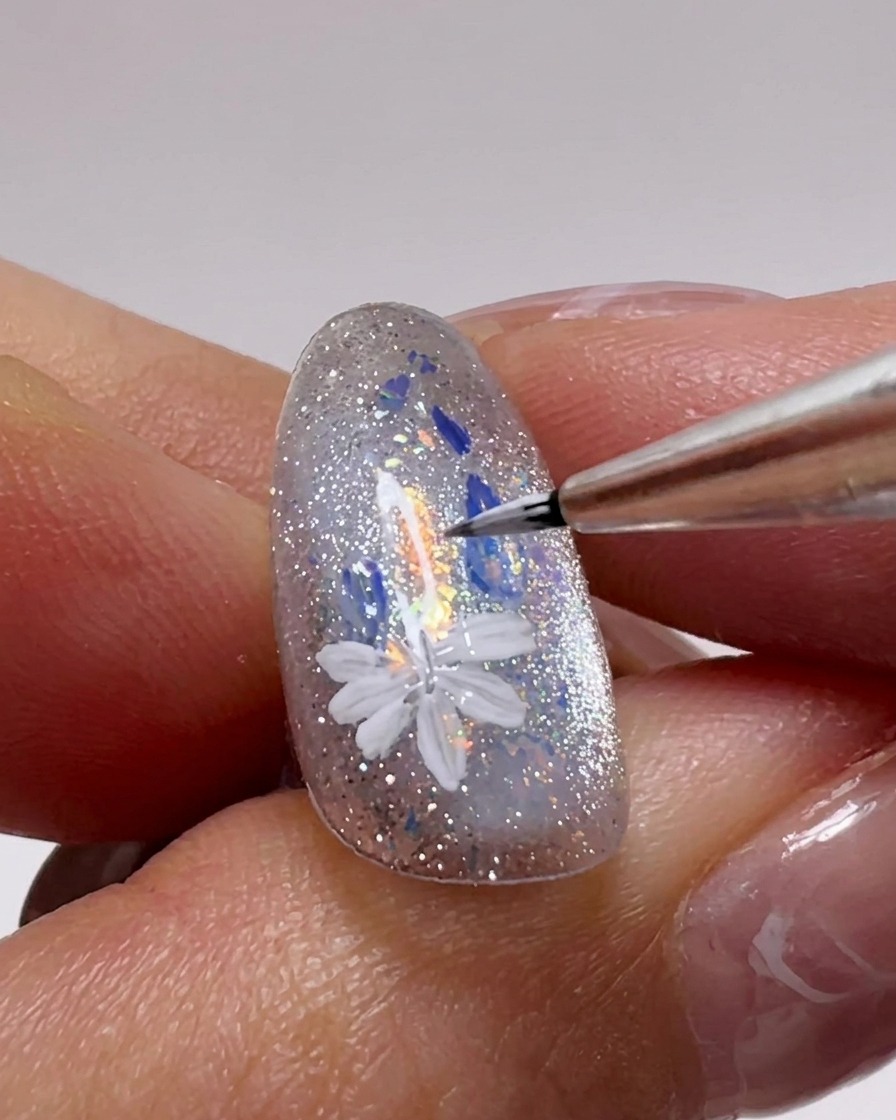 Close-up of a nail showing multiple white daisy flowers being painted onto the surface with a fine detail brush.