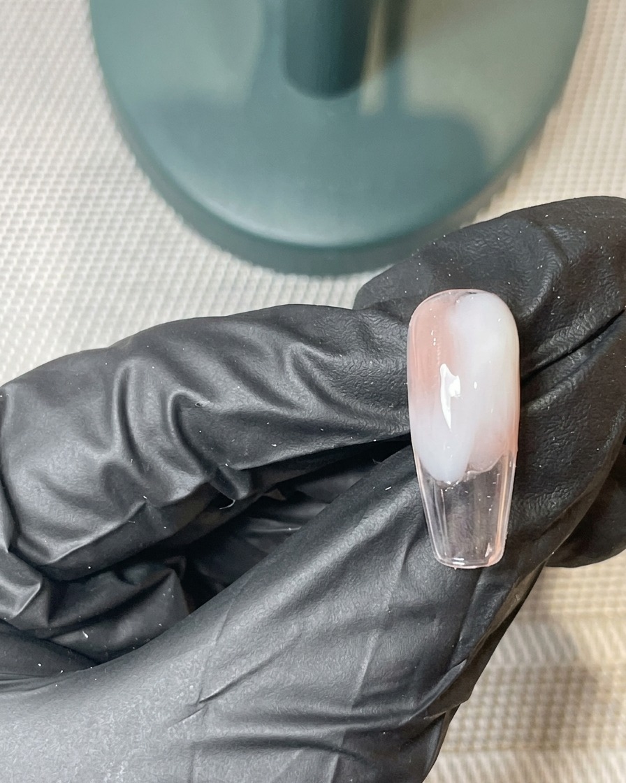 A brush applying a second thin layer of pink and white gel over the previously cured ombre base.