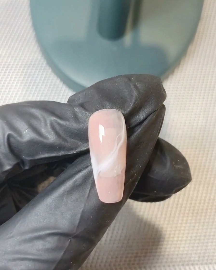 A gel brush perfecting the blend of the second gel layer on the nail.