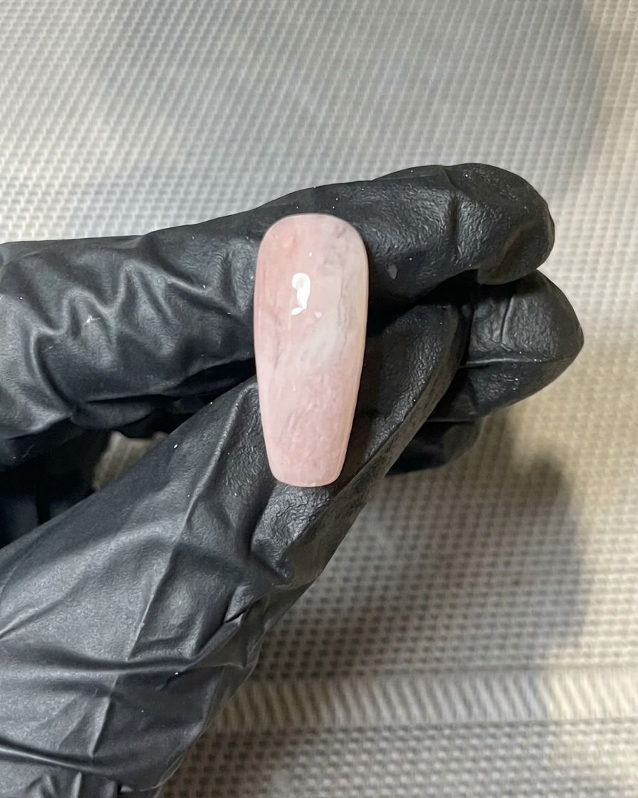A close-up of gold foil flakes being pressed onto the tacky surface of a gel-painted nail.