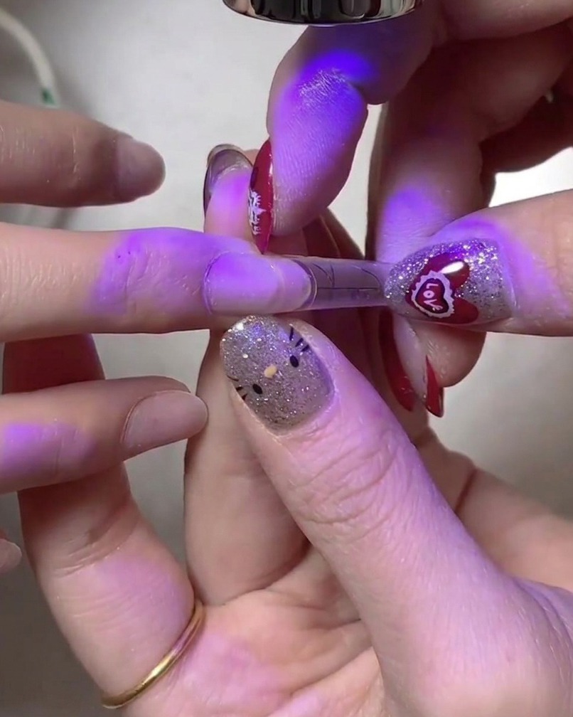 A hand holding a nail under a secondary UV/LED lamp light for thorough curing.
