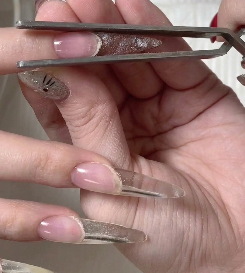 Metal tweezers carefully lifting the plastic form away from the surface of the newly cured nail.