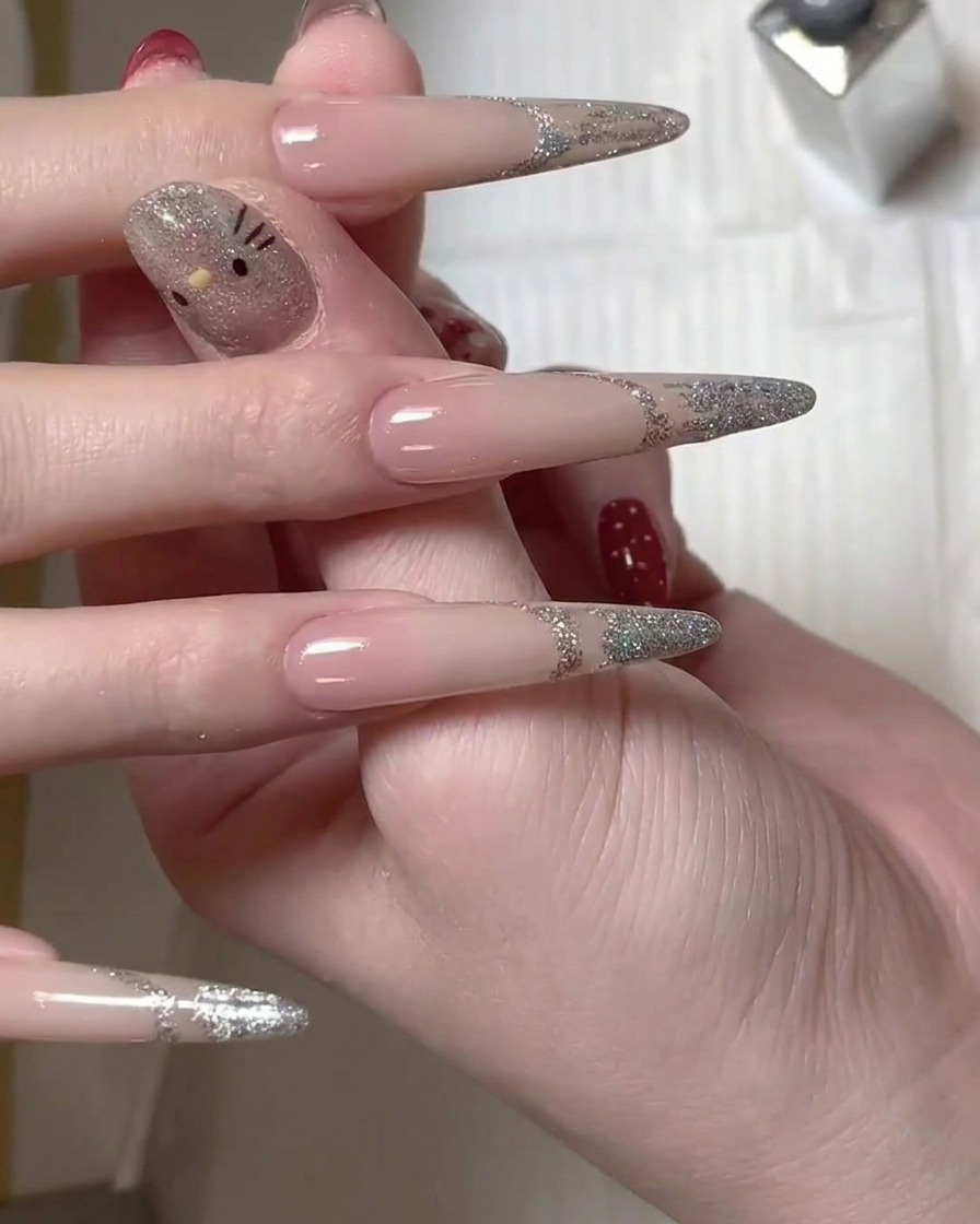 A brush applying silver glitter gel polish to the tip of a long nail to create a french manicure design.