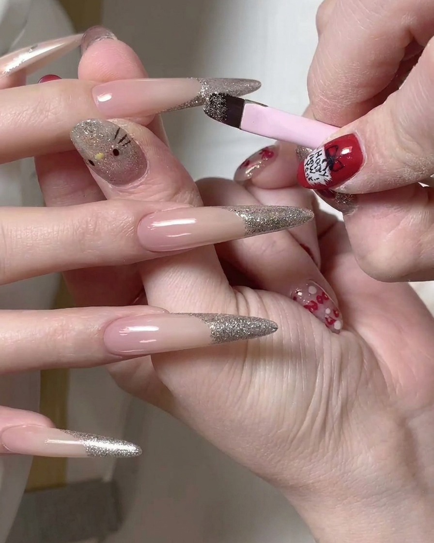 A detail brush being used to clean up the edge of a silver glitter french tip on a long nail.