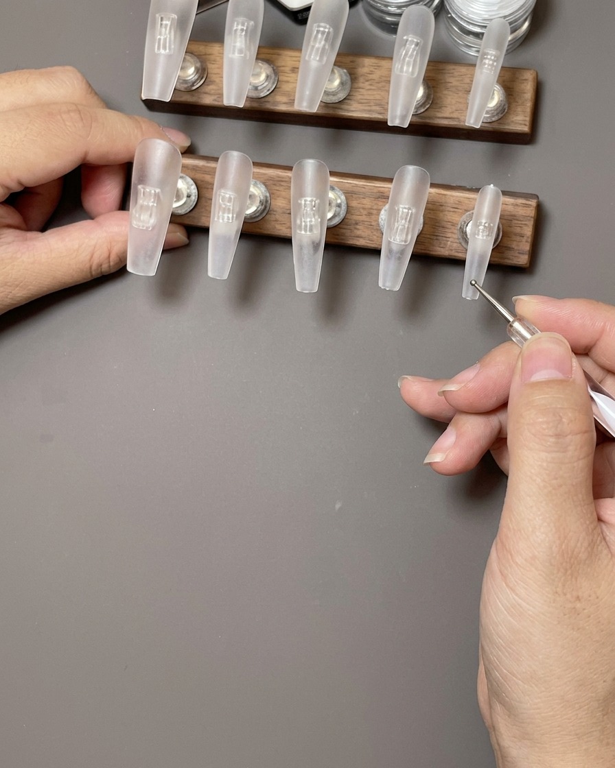 A hand using a lint-free wipe to clean the surface of a clear press-on nail.
