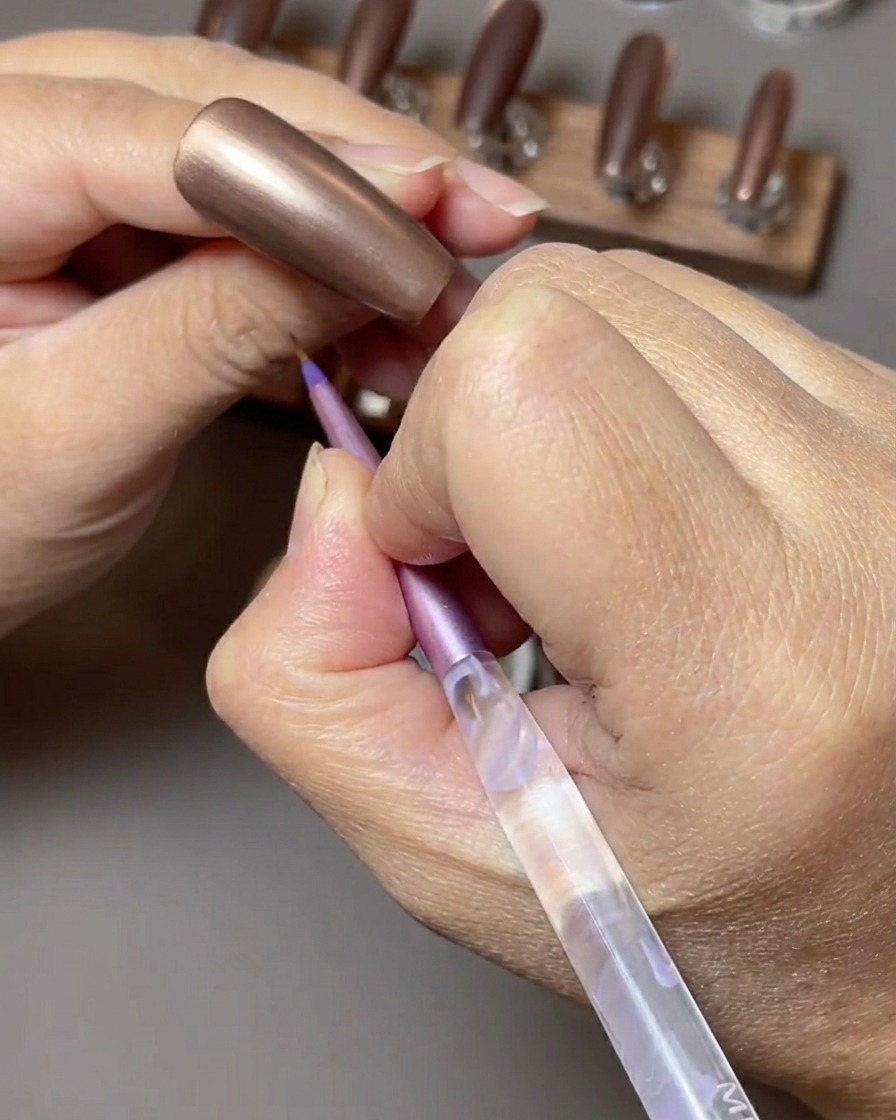 A brush applying a rich, toffee brown cat-eye gel polish onto a nail.