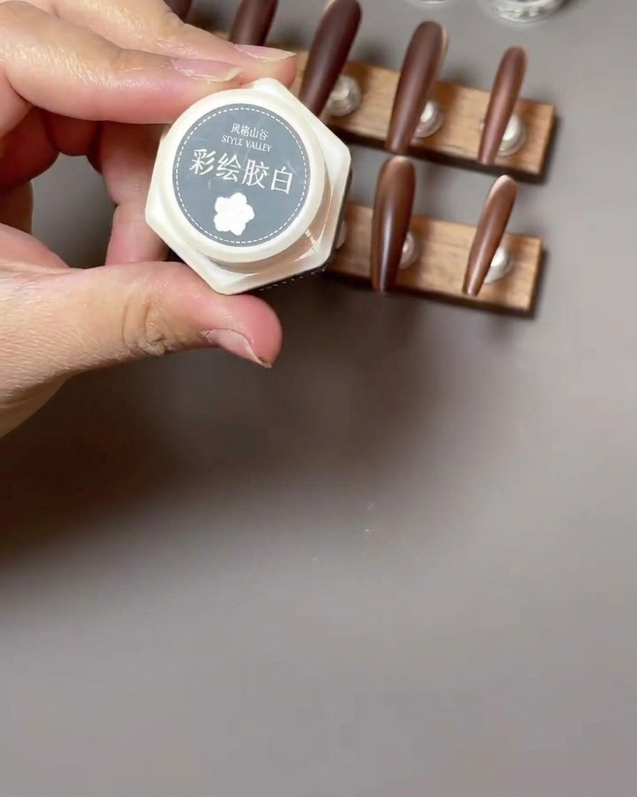 A fine liner brush drawing white, delicate, parentheses-shaped petals for a rose design on a matte brown nail.