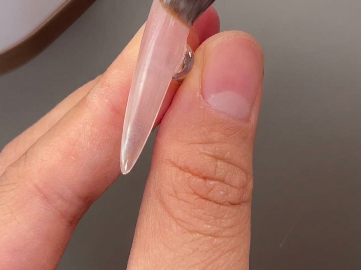 A brush applying a clear layer of base gel onto a natural nail.