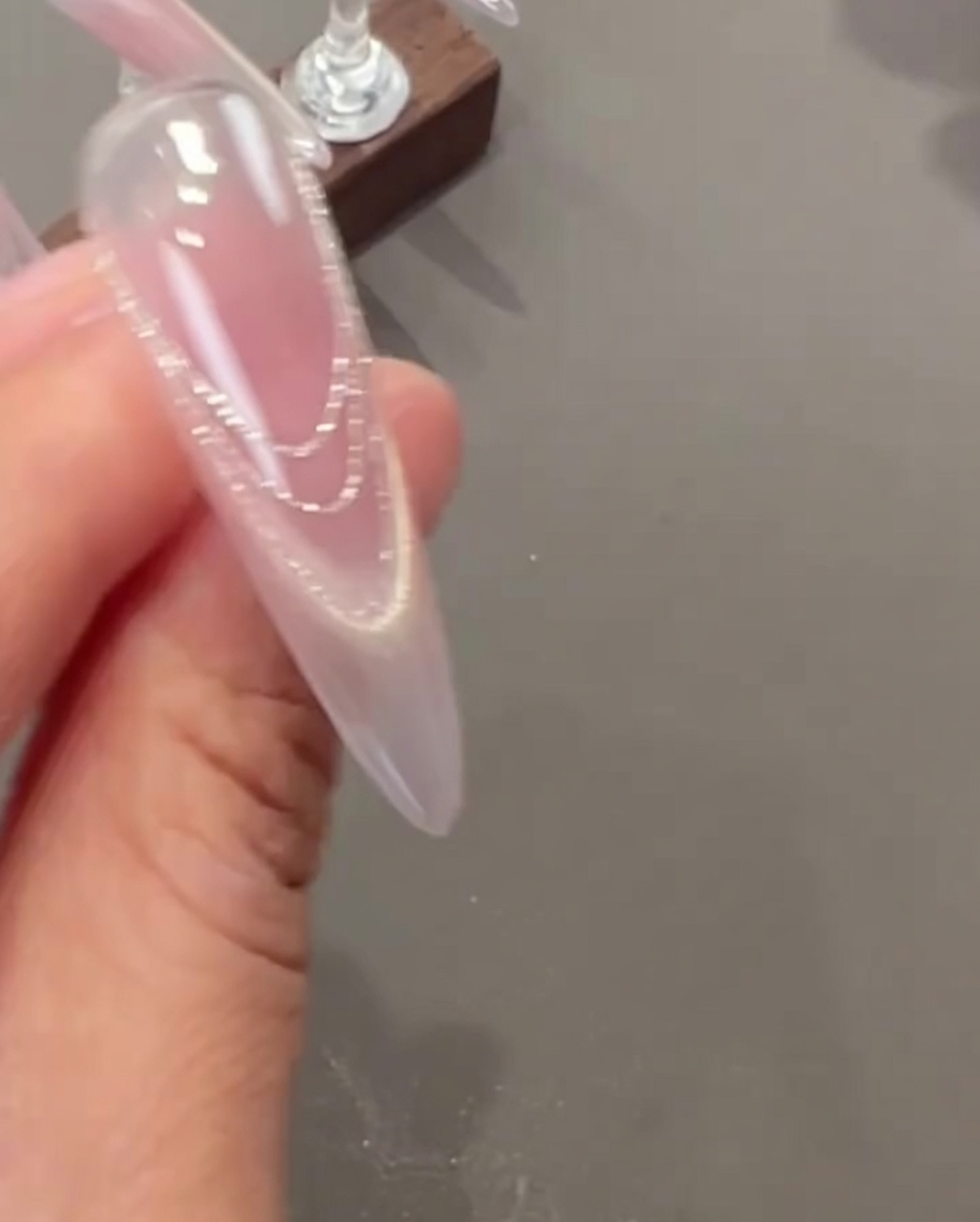 Tweezers applying small, delicate dried flowers and tiny pearl charms onto a fingernail.