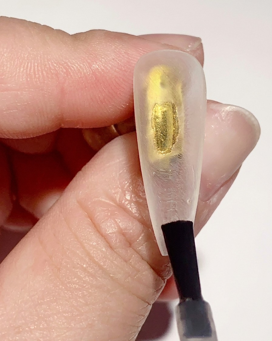 A brush applying a thin layer of clear gel base coat to the inner surface of a clear nail tip.