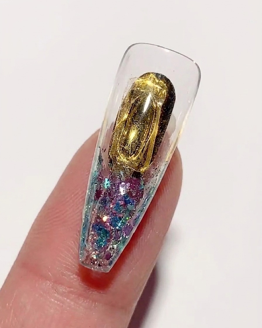Applying a clear, thick hard nail glue over the gold-colored inner surface of a nail tip.