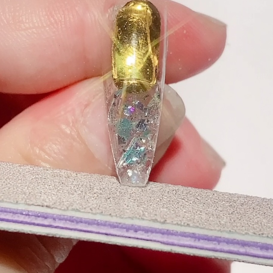 A nail file refining the edges of a textured nail tip to ensure a smooth perimeter.