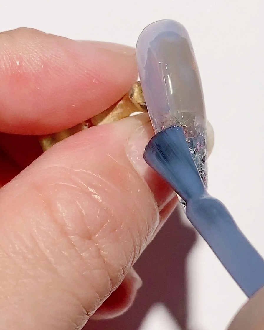 A gradient brush blending sheer blue gel polish on the nail surface for a smooth transition.