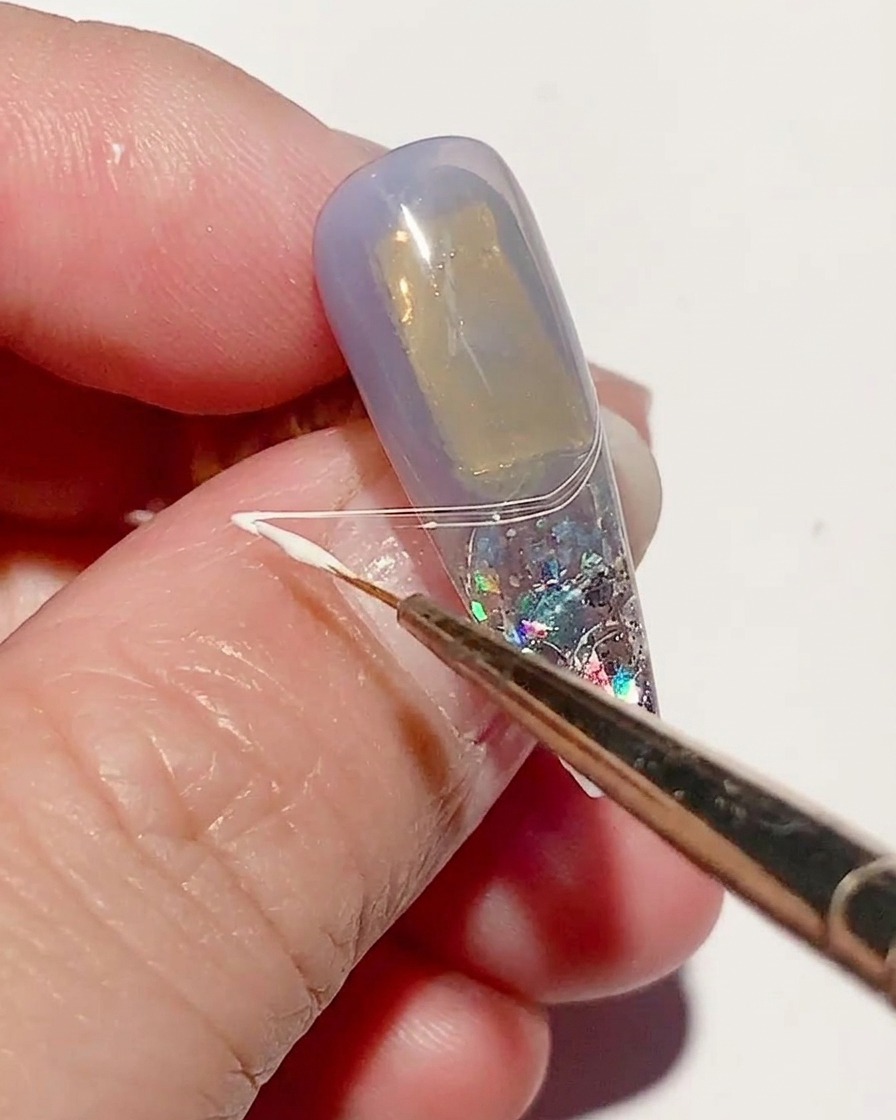 A fine liner brush stretching white spider gel across the nail surface to create thin, web-like lines.