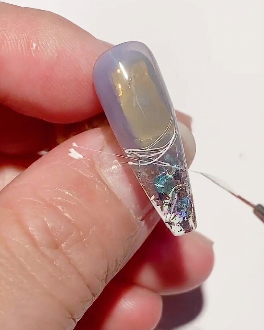 A close-up of a nail with white spider gel lines being cured under a UV nail lamp.
