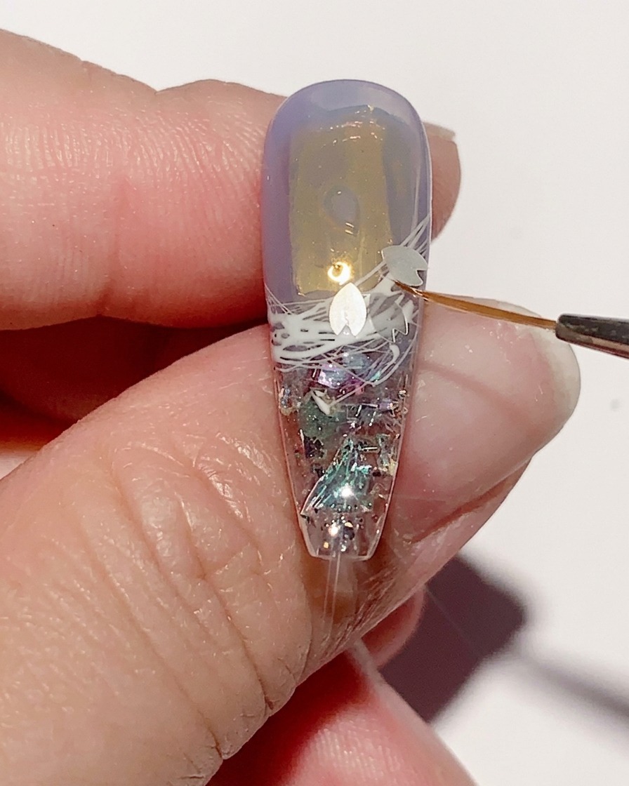 Tweezers placing small, delicate cherry blossom-shaped sequins onto the wet gel surface of a nail.