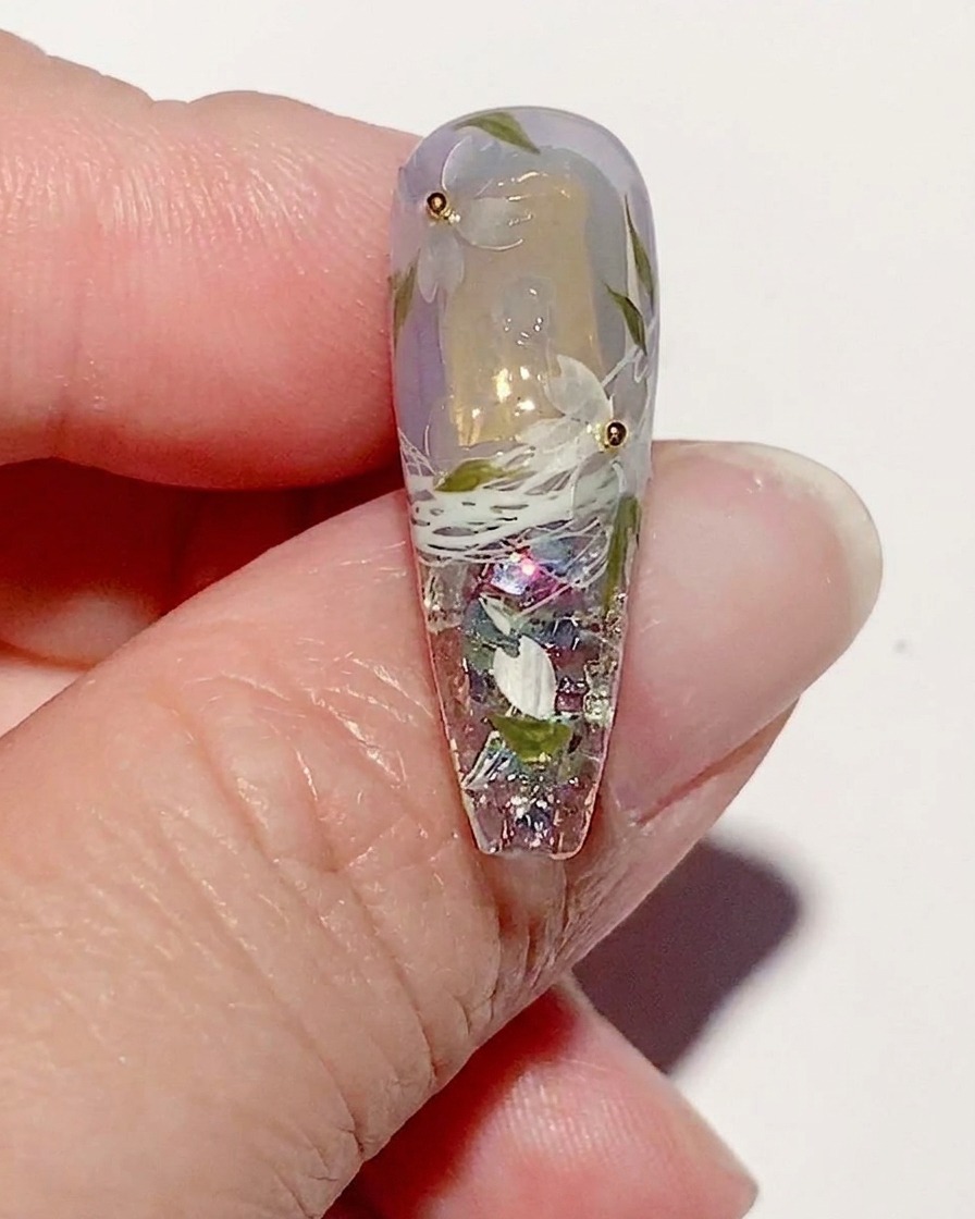A manicured nail with cherry blossom art, showing a glossy top coat being applied over the entire design.