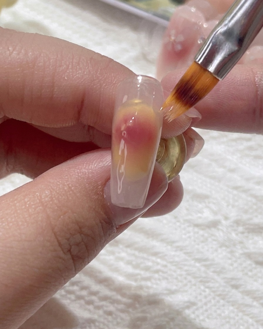 A small brush gently blending the pink gel on the nail surface.