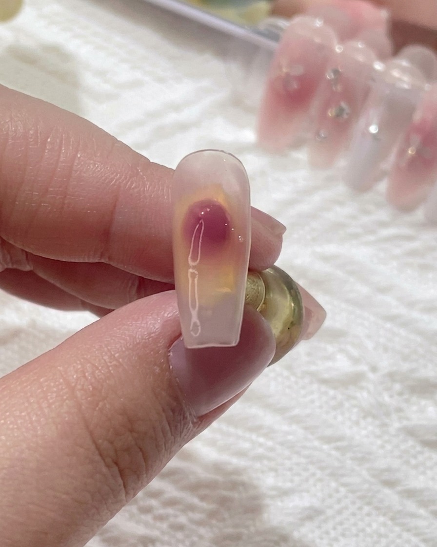 A close-up shot of a nail brush blending a pink gel dot on a clear nail to create a soft blush gradient.