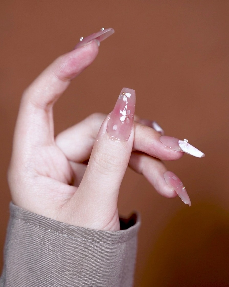 A brush applying a clear, thick adhesive gel to a nail with a pink gradient base.