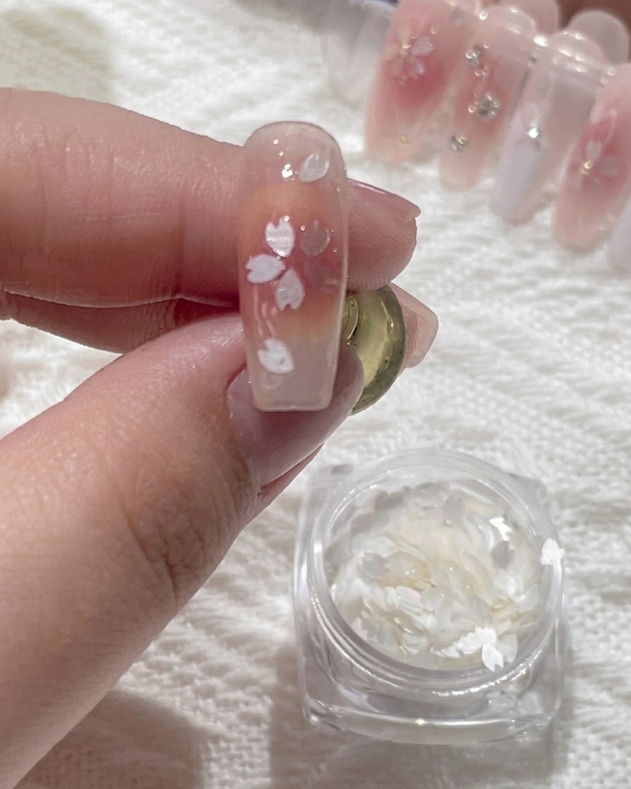 A precision tool applying a tiny bead of clear glue to the center of a floral nail art design.