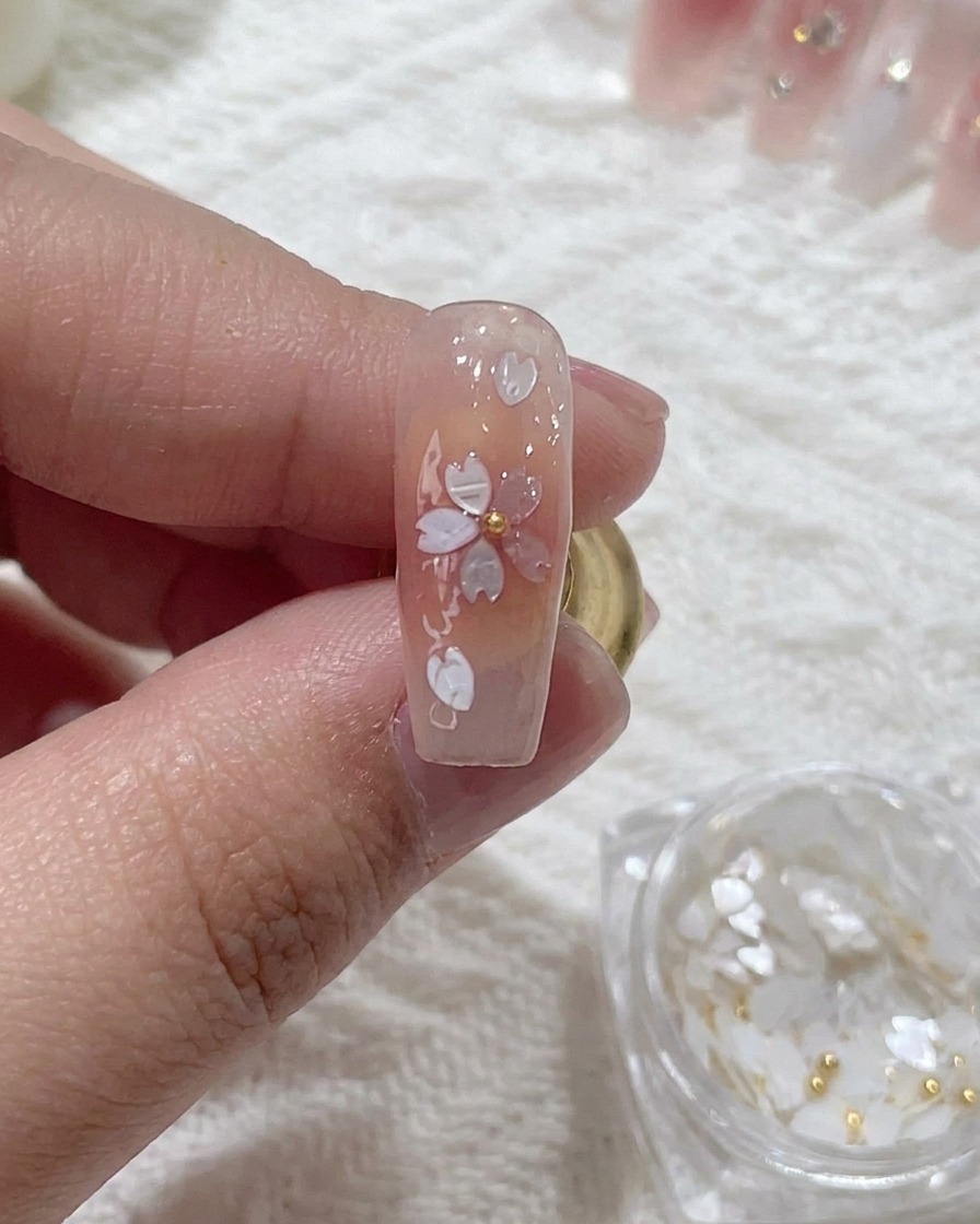 Close-up of a metal bead being pressed into the center of a cherry blossom sequin nail design.
