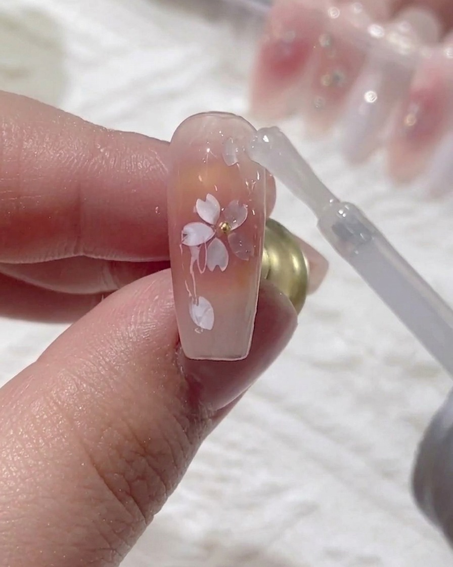 A brush applying a final, high-gloss top coat over the encapsulated cherry blossom design.