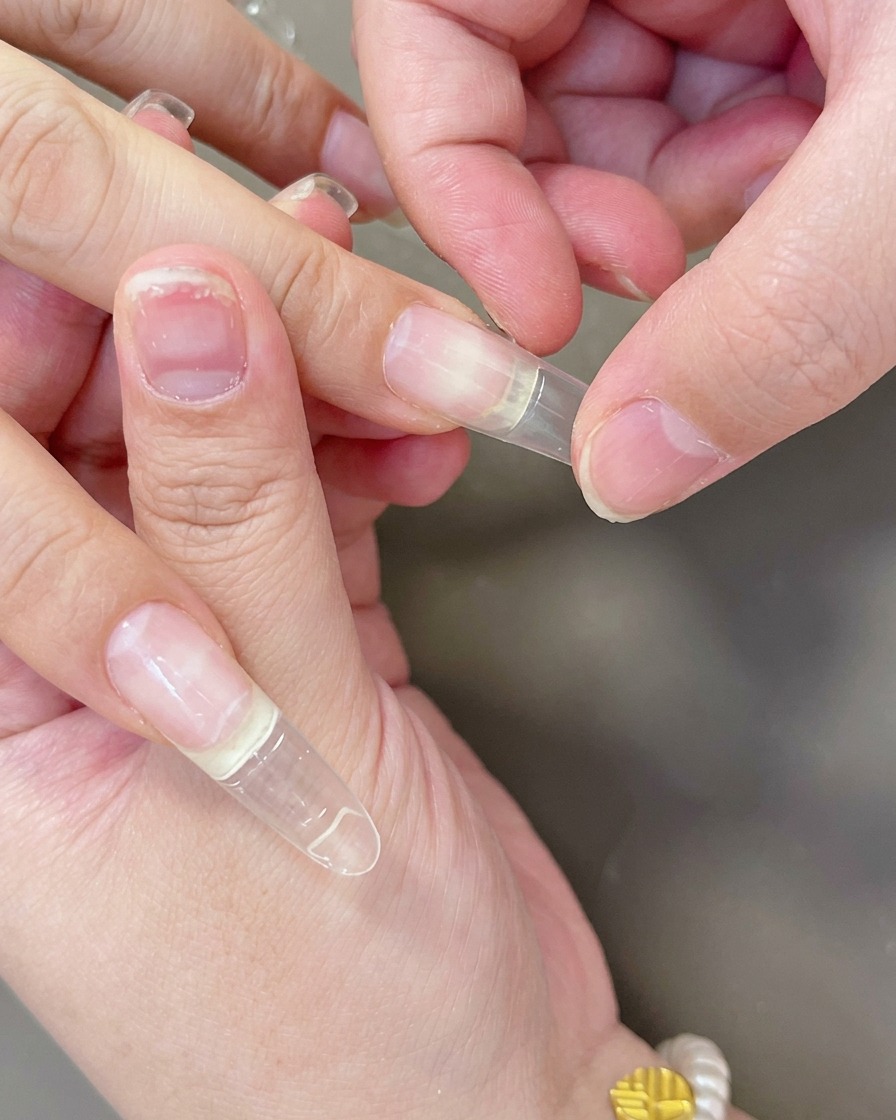 Fingers pressing a clear gel extension tip down onto the nail bed to ensure it adheres correctly.