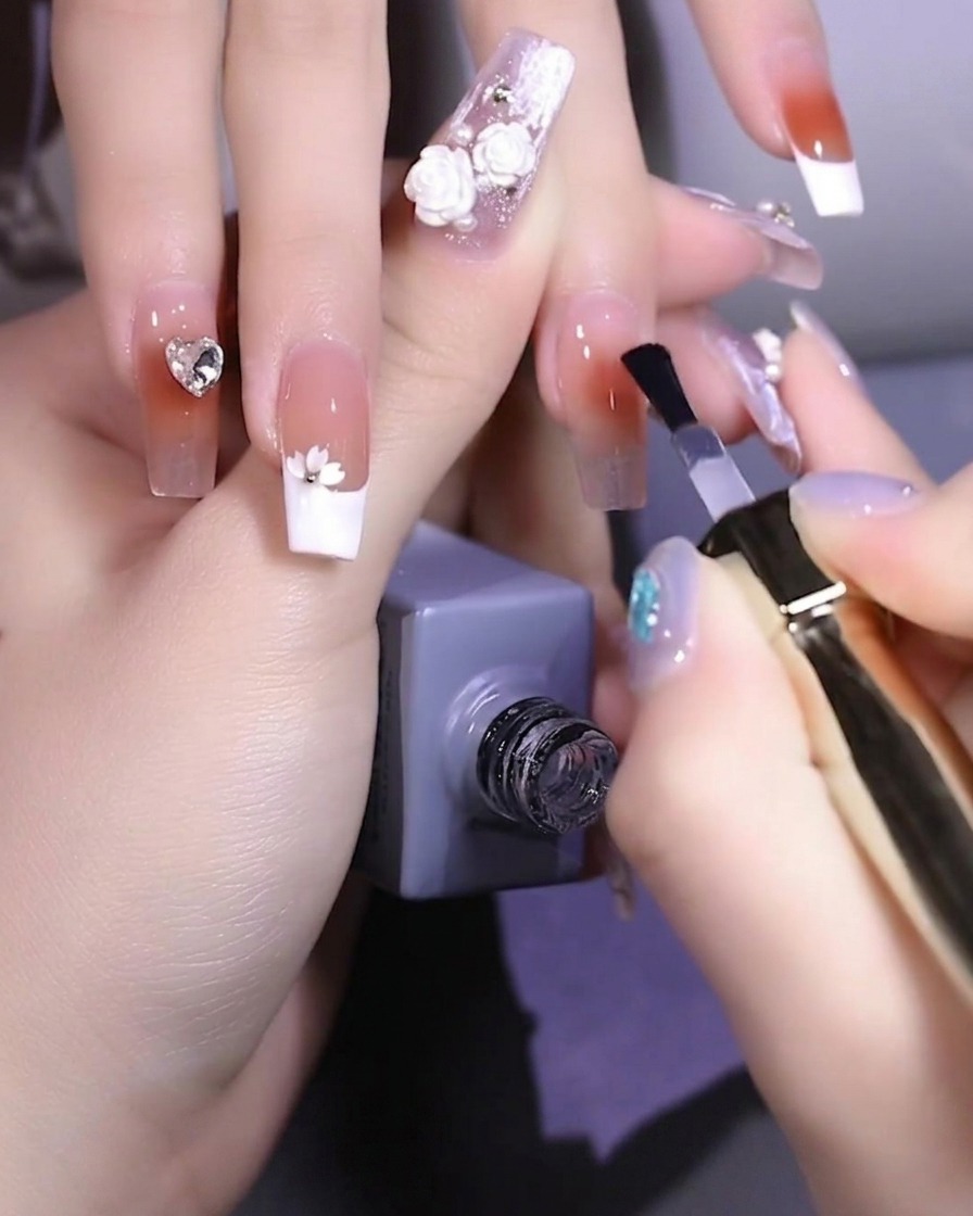 A nail brush applying clear strengthening base gel to a natural fingernail.