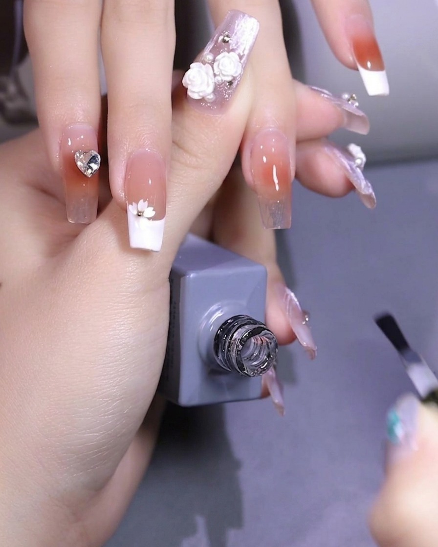 Tweezers placing a small, white cherry blossom-shaped sequin onto a nail surface.