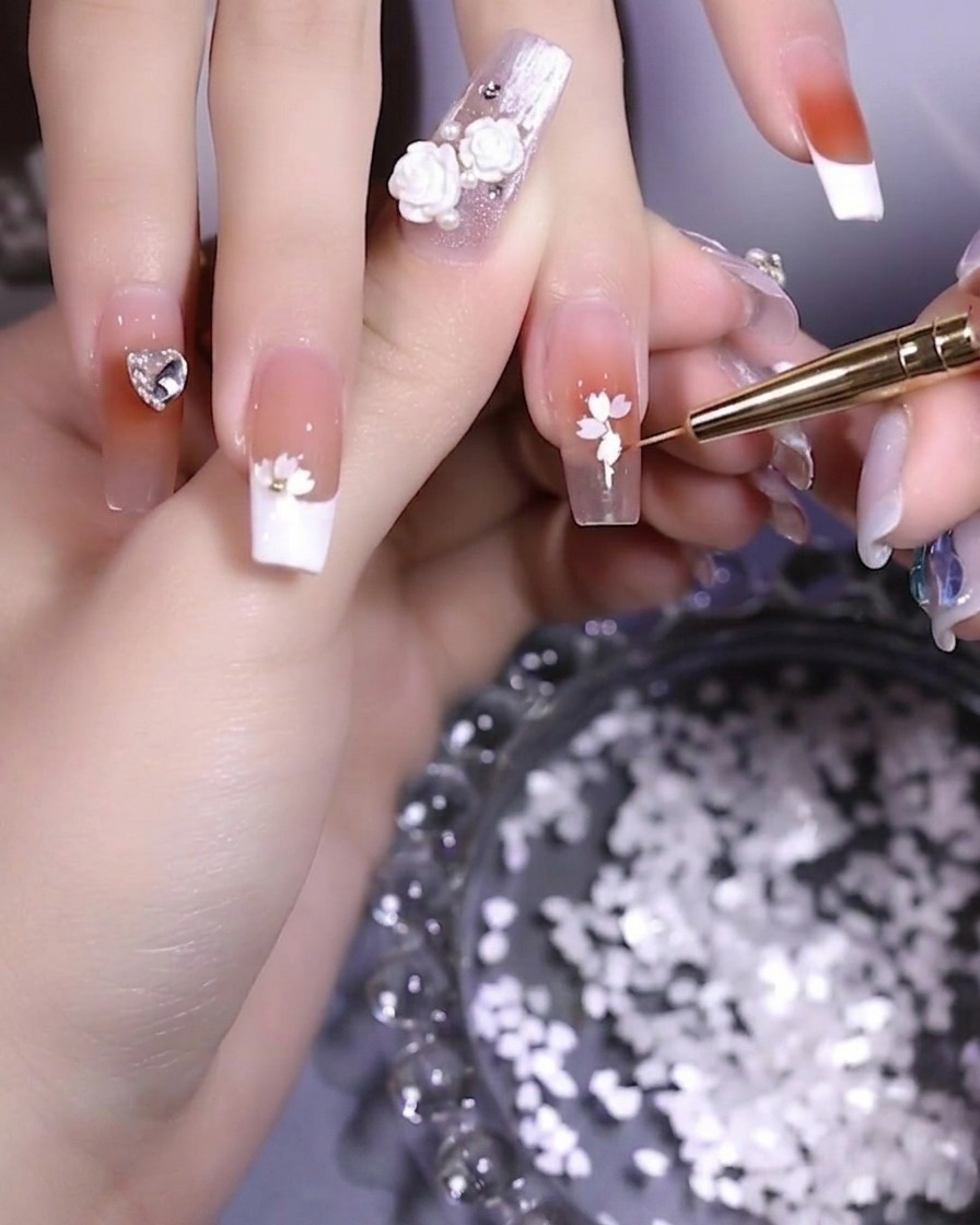 A close-up of a nail showing petals being arranged into a flower shape with tweezers.
