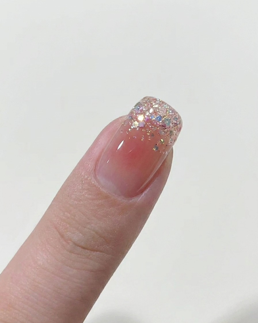 A brush applying a thin layer of nude gel polish to a bare nail.