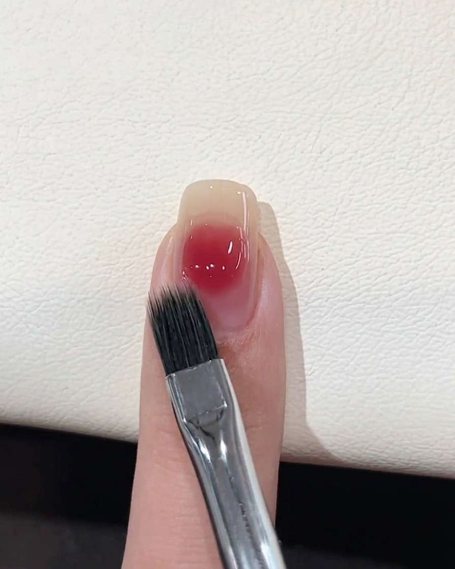 A flat blending brush softening the edges of a pink gel dot on a nail.