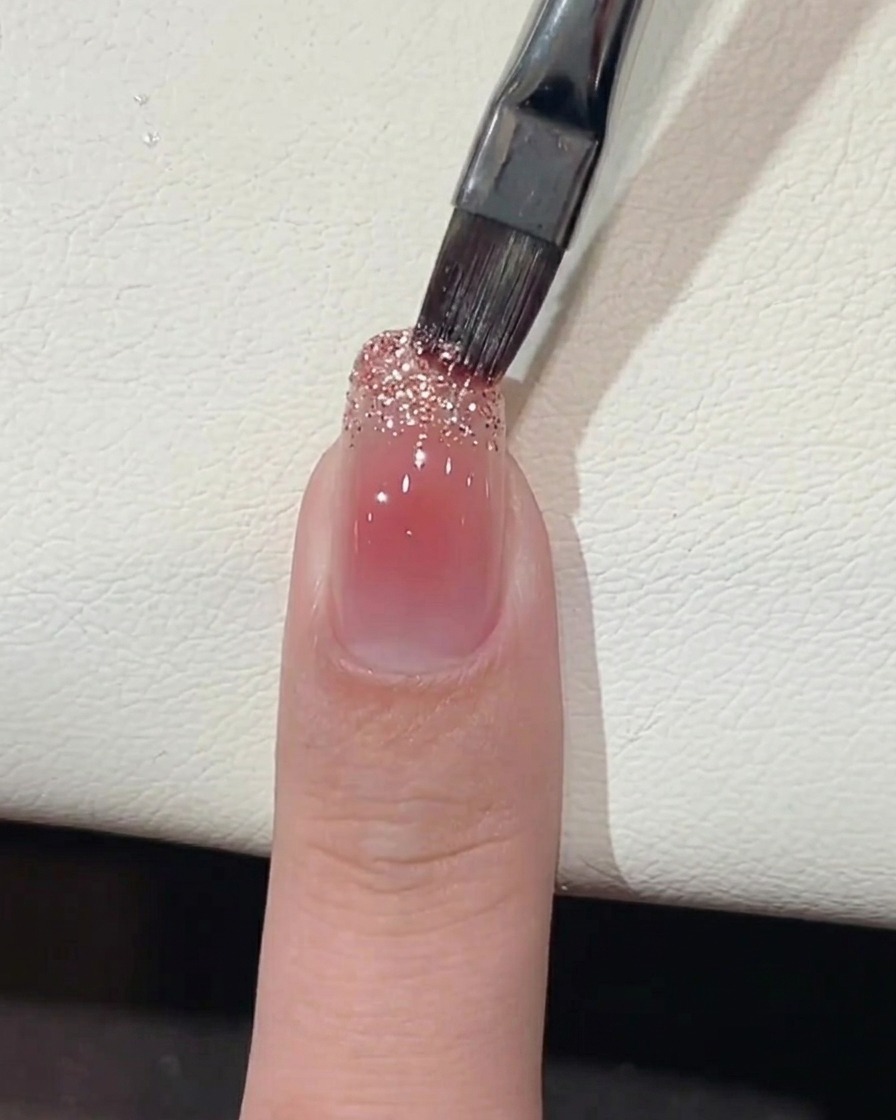 A brush applying chunky glitter gel to the free edge of the nail.