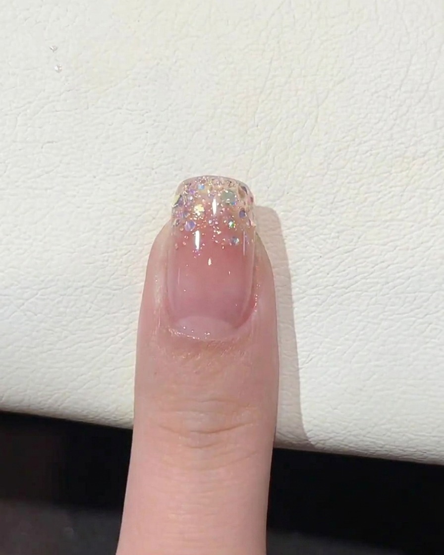 A brush applying a clear, glossy top coat over the glitter-gradient nail tip.