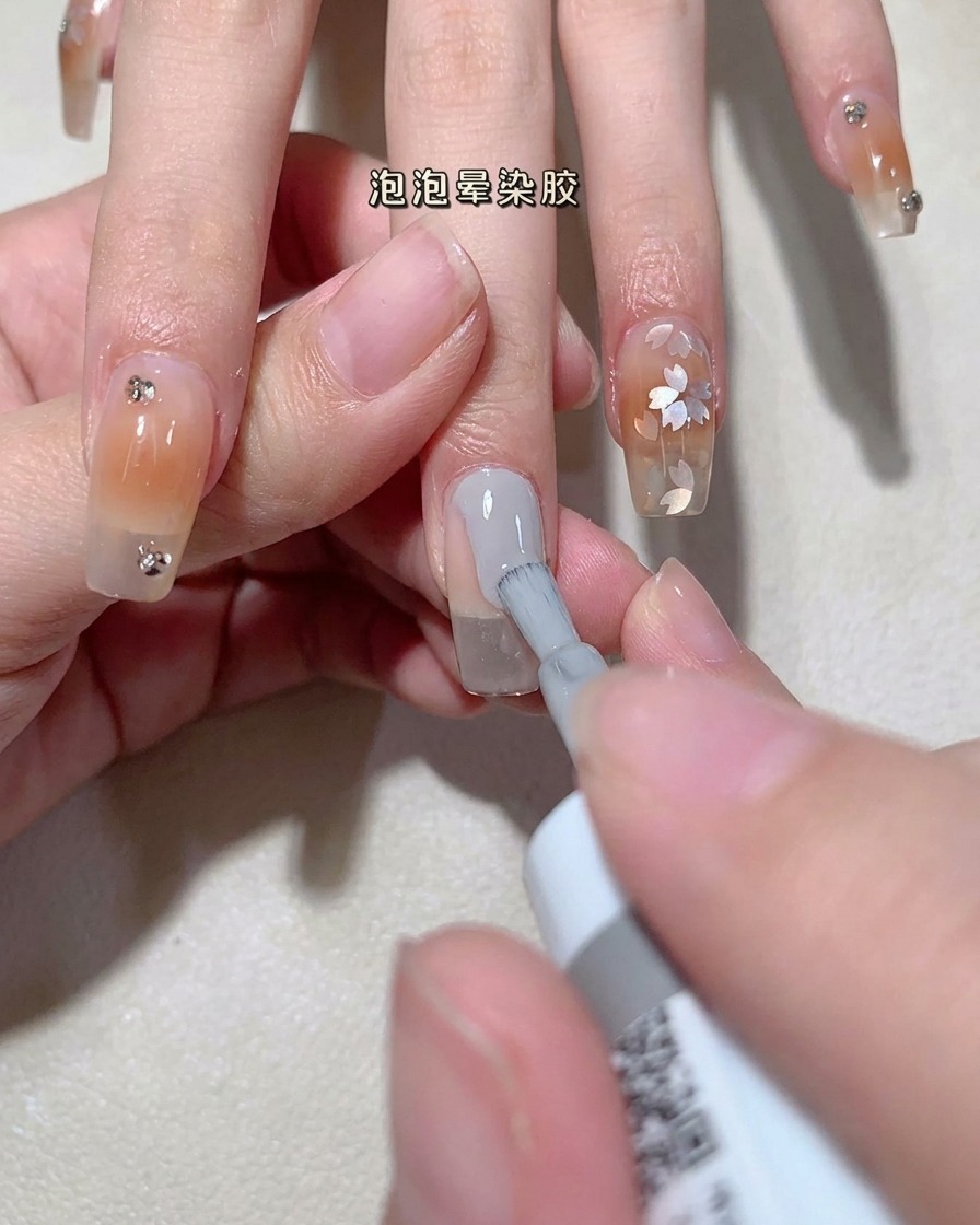 A close-up view of a brush applying clear bubble gel onto a natural nail plate.