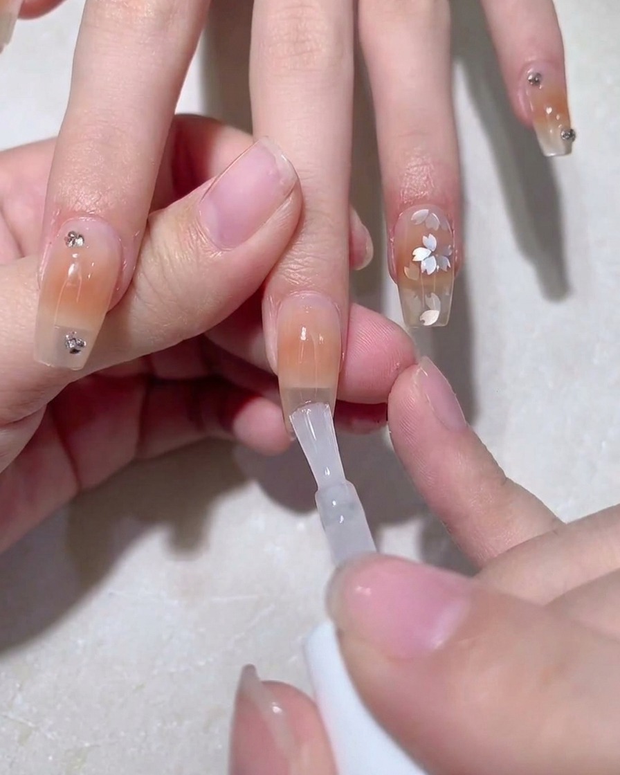 A brush applying a thin layer of clear adhesive gel over the ombre nail surface.