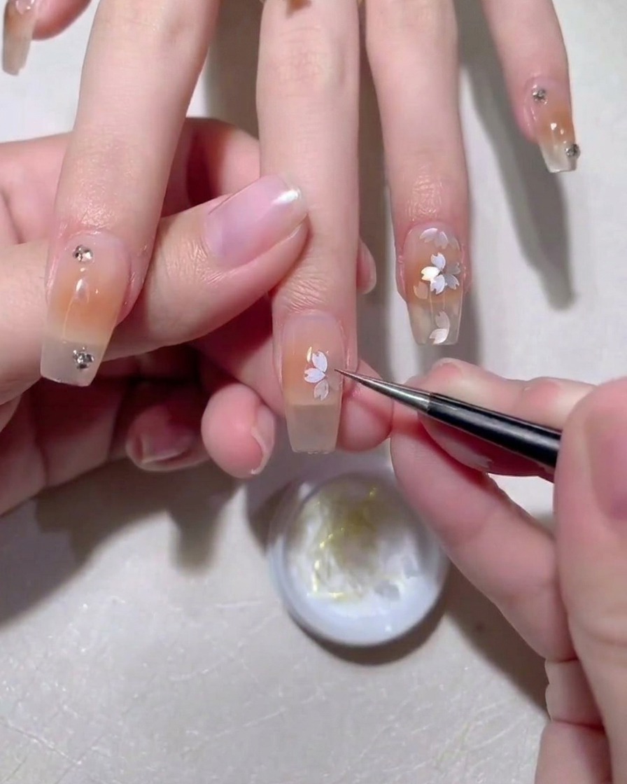 Tweezers placing a sakura petal sequin onto a nail surface covered in wet gel.