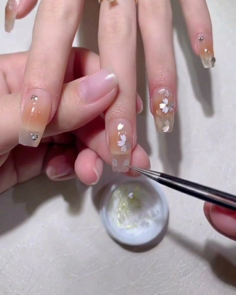 A close-up of a nail with petal-shaped embellishments being accented with a fine brush and brown gel.