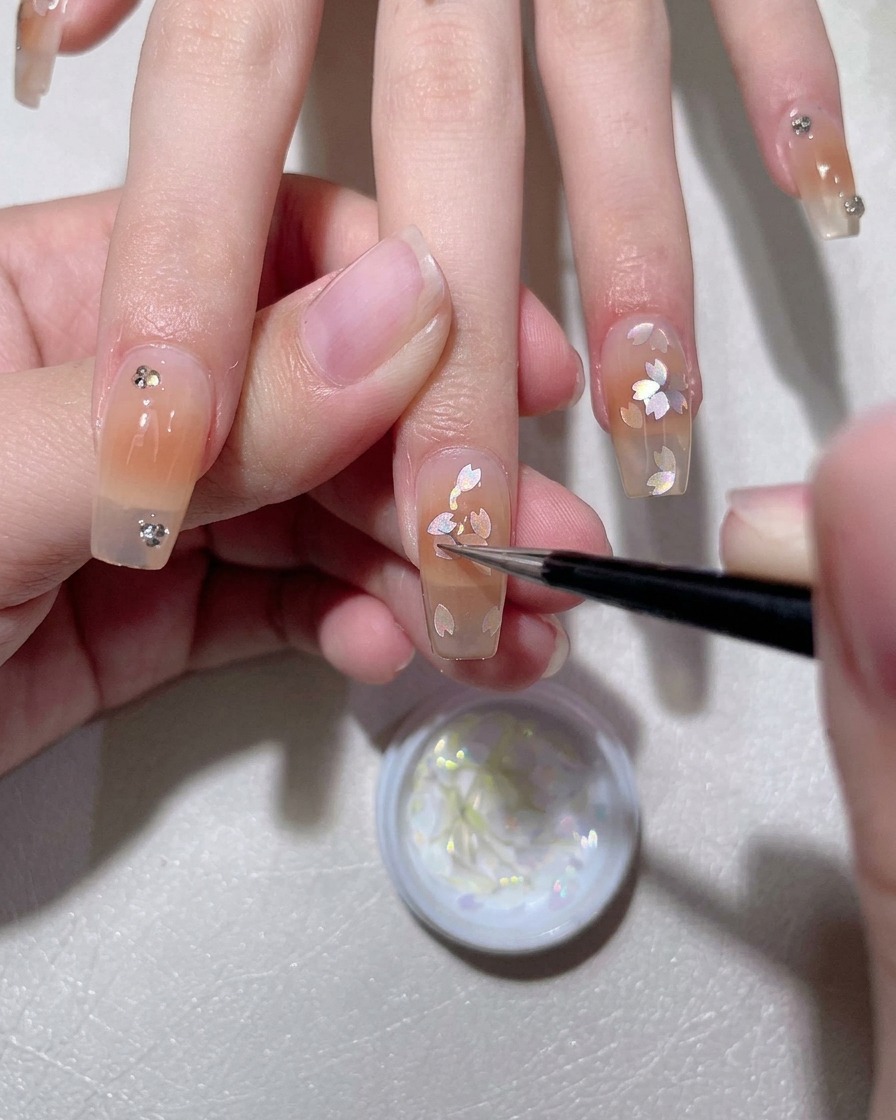A brush applying a milky white gel base coat onto a natural fingernail.