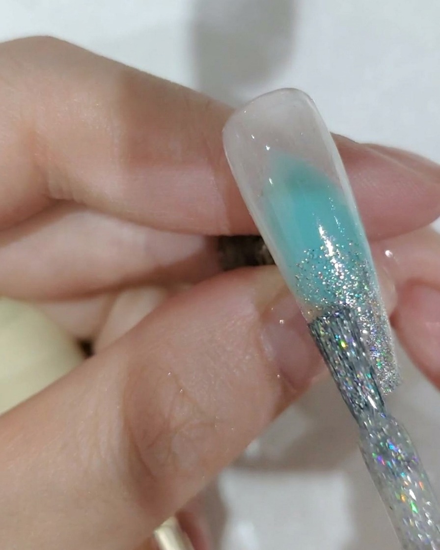 A close-up of a nail brush applying silver glitter gel to the tip of a nail.