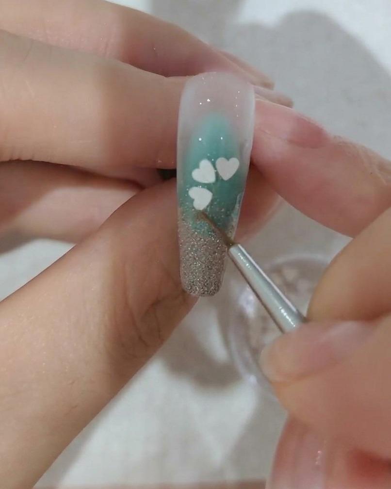 A close-up view of a nail being decorated with a third white cherry blossom sequin petal.