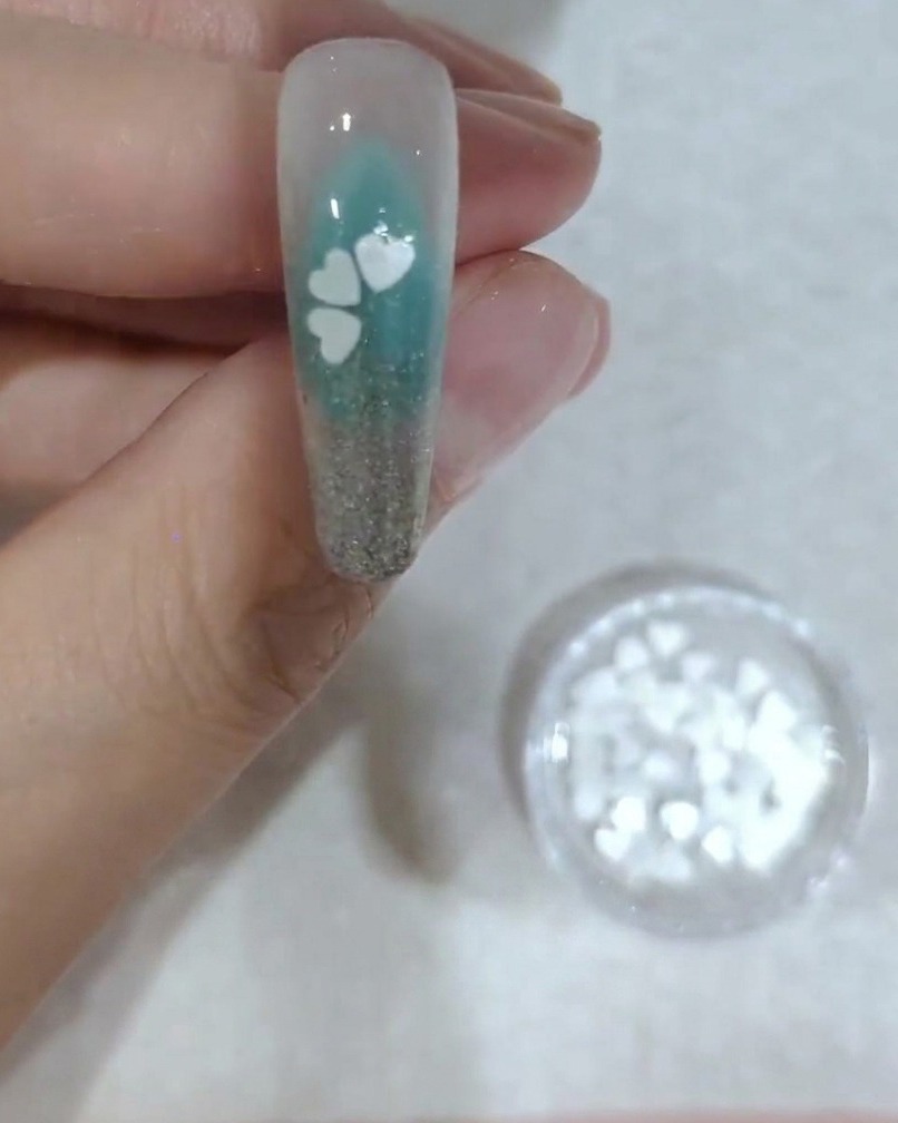 A close-up view of a nail showing the placement of the fourth white cherry blossom sequin petal.