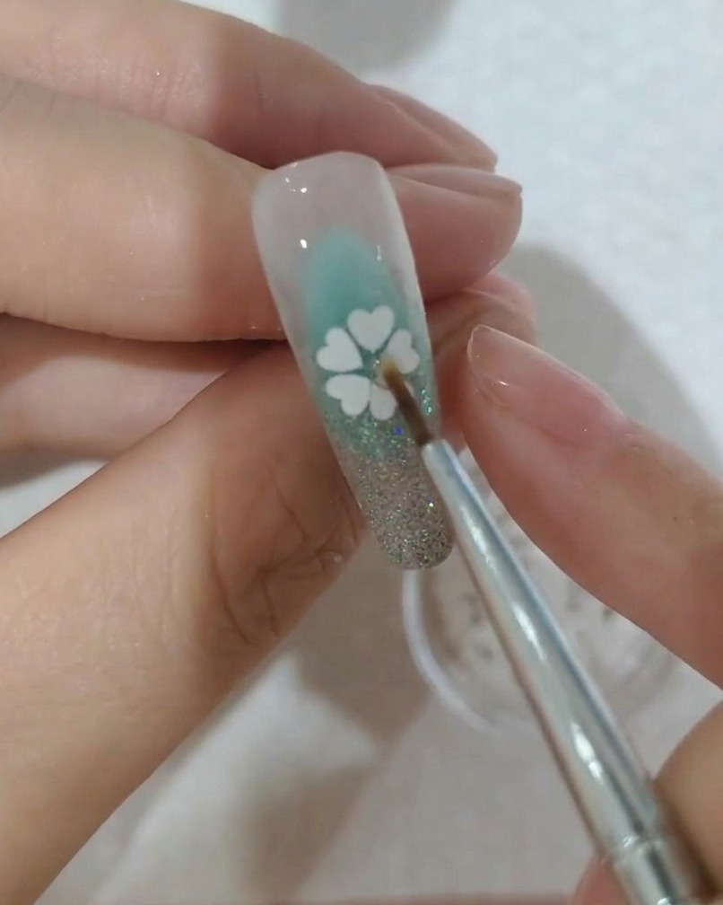 A close-up view of a small crystal being placed in the center of the sequin flower on a nail.