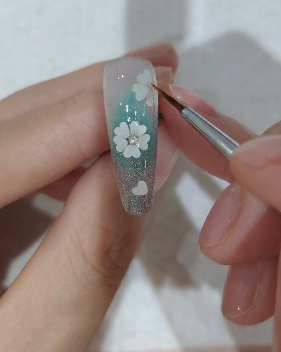 A close-up of a decorated nail with crystals being placed under a professional UV nail lamp for curing.