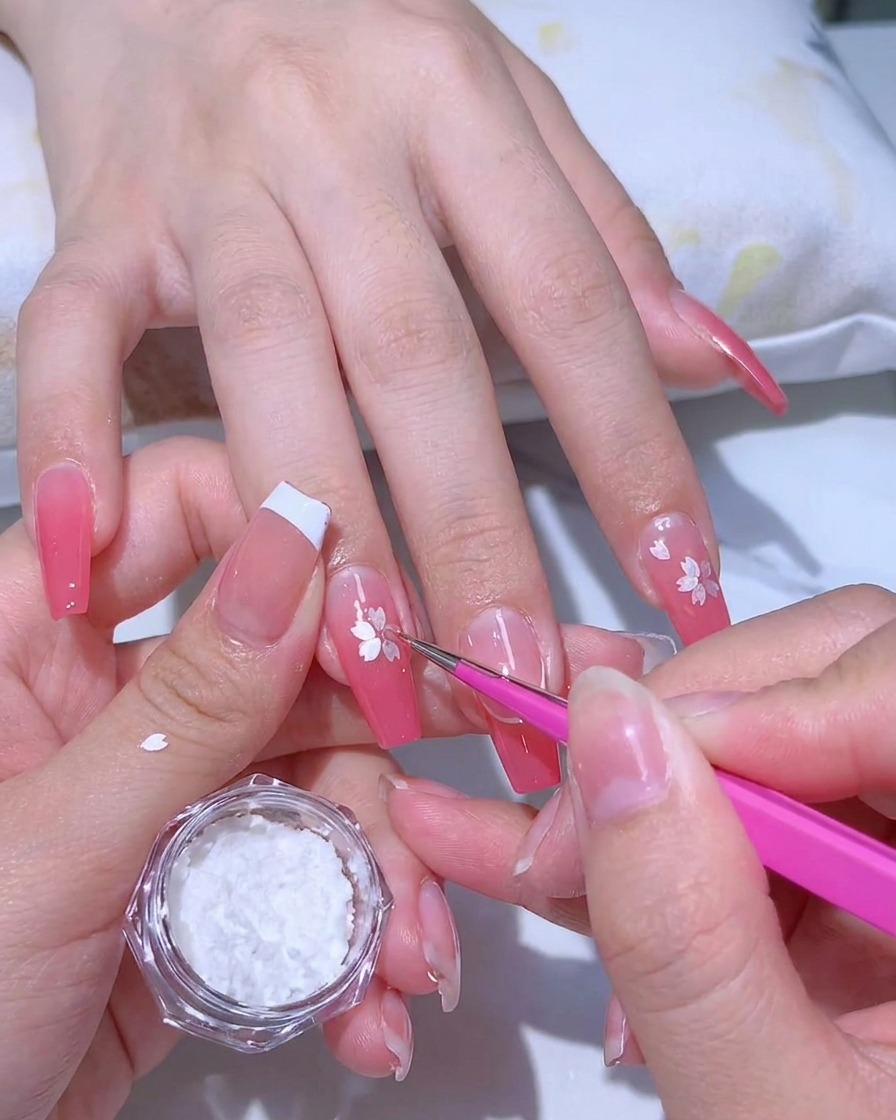 Applying a clear, sticky adhesive gel over a pink gradient manicure with a fine-tipped brush.