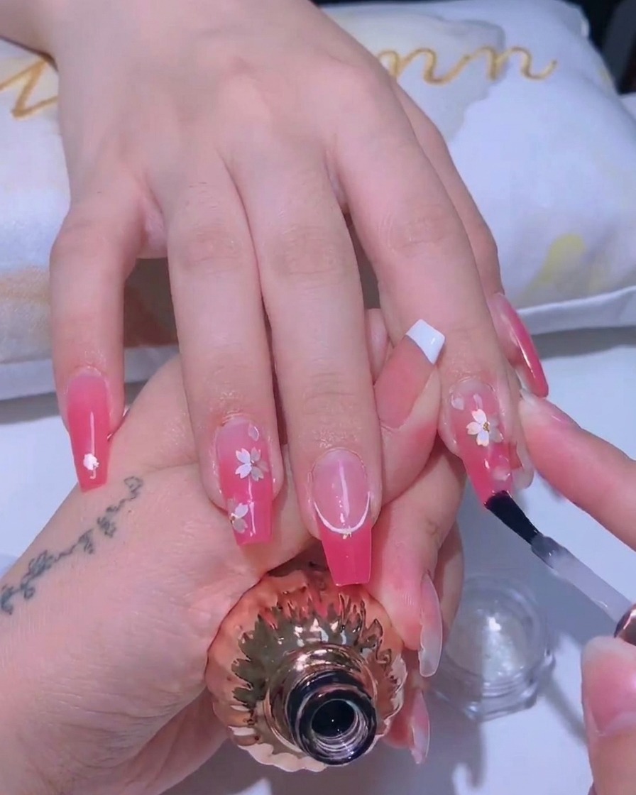 A nail brush applying a thin, glossy top coat over a cherry blossom nail design.