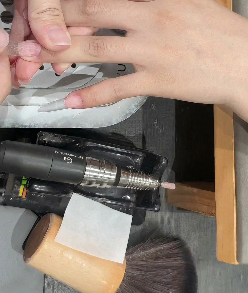 A close-up view of a clear plastic nail tip being applied to a natural fingernail.
