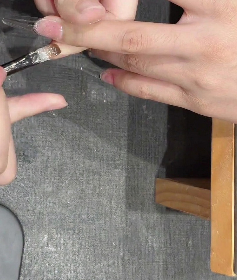 Tweezers placing small, metallic star-shaped glitter pieces onto a wet gel-coated nail.